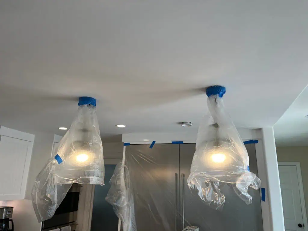 Ceiling painting in progress with protective plastic coverings and lighting fixtures.