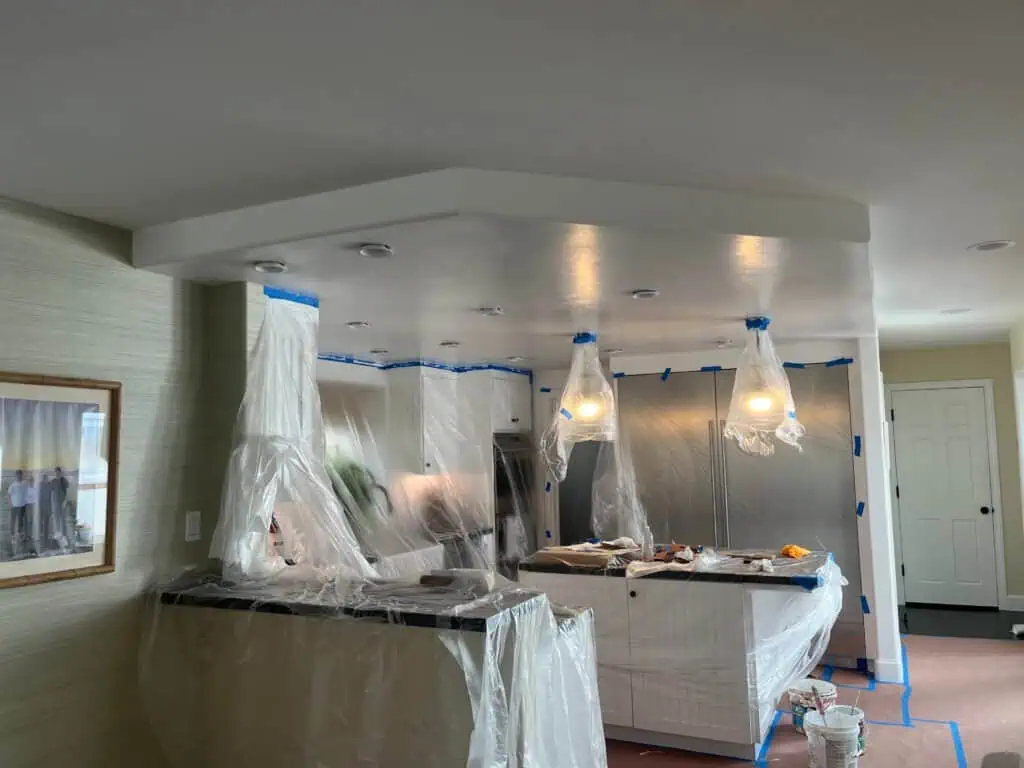 Professional interior painting with protective plastic coverings and modern lighting.