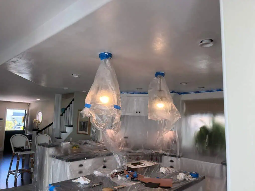 Professional interior painting with plastic coverings and lighting fixtures protected.