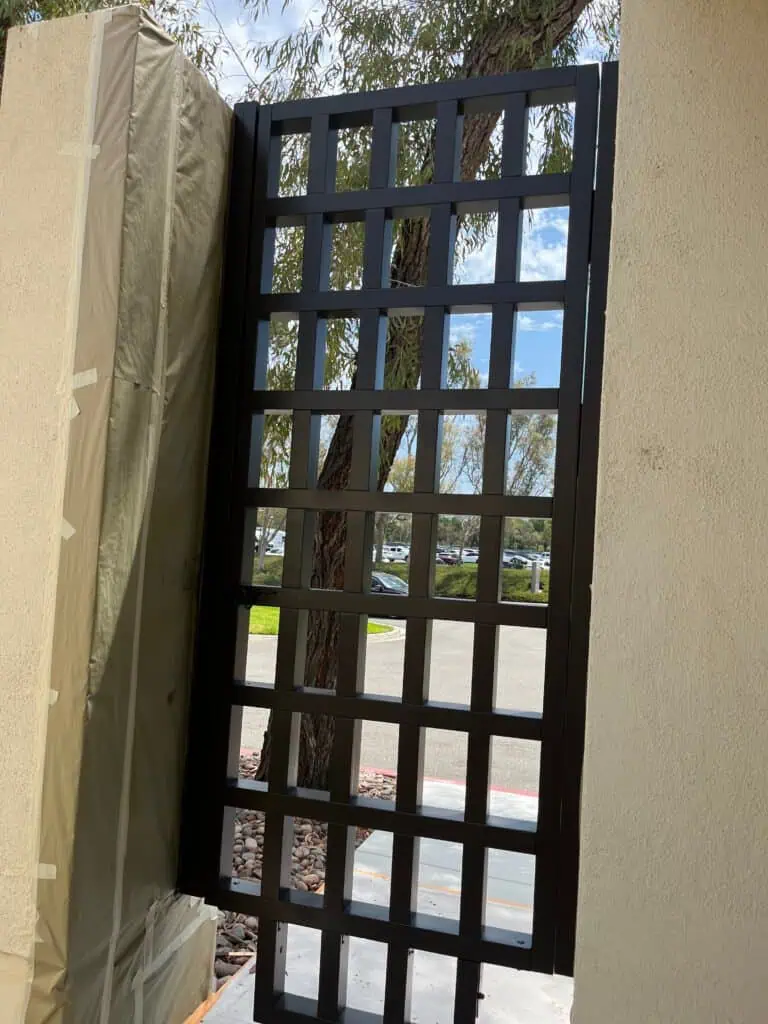 Freshly painted black grid door outside a building with trees in background.